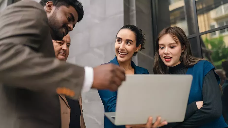 Colleagues collaborating around a laptop during a business meeting in a modern office setting