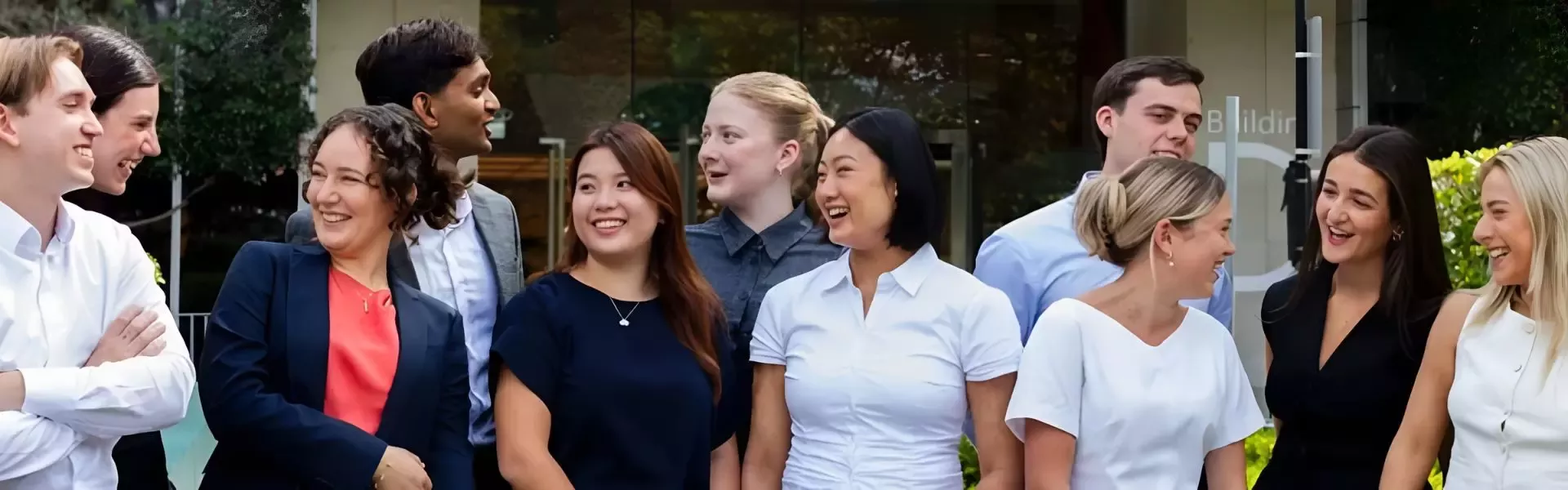 Diverse group of coworkers smiling and chatting outside a modern office building.