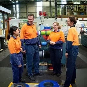 Employees in a manufacturing facility discussing work beside production equipment
